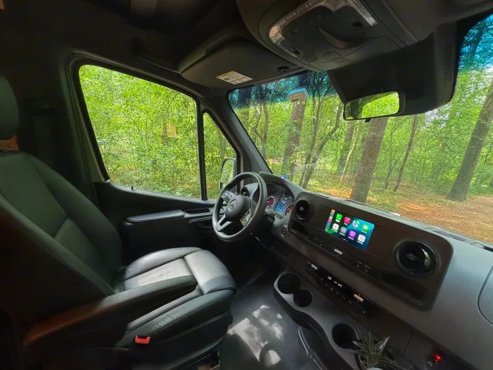 RV rental interior: modern van cockpit, infotainment screen, comfy seat, and lush forest outside.. Mercedes-Benz Sprinter RV Motorhome Campervan 2022