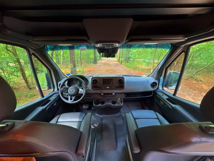 RV rental van interior: dashboard, seats, and forest road view. Ready for your next adventure or road trip.. Mercedes-Benz Sprinter RV Motorhome Campervan 2022