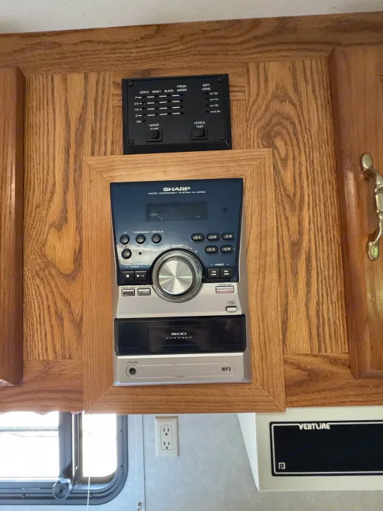 RV rental interior showing a water/battery level monitor and a Sharp stereo system integrated into wood cabinetry.. Forest River Wildwood 2000