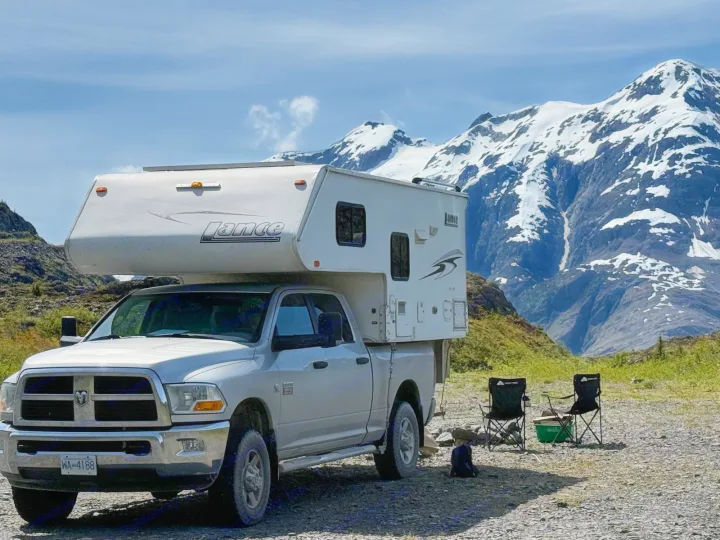 This RV rental, a truck-mounted camper, is parked in a rugged mountain landscape with two camping chairs set up.. Dodge RAM 3500HD 2010