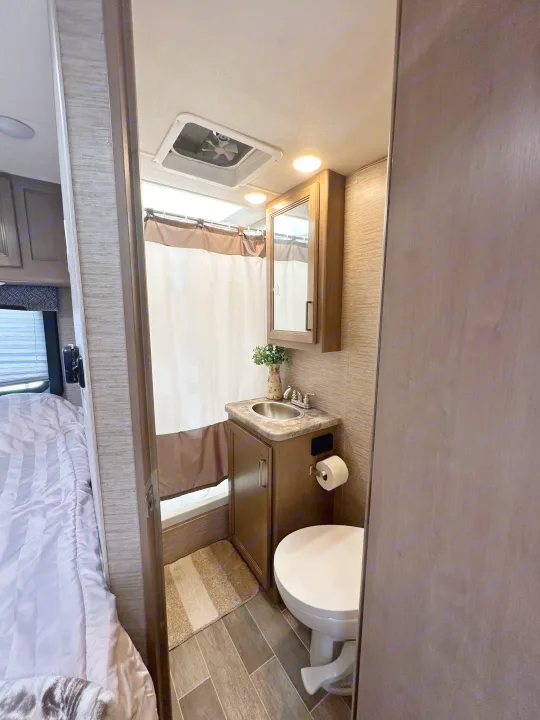 Compact RV rental bathroom with shower, sink, and toilet, showing its efficient layout and bedroom access.. Thor Chateau 2022