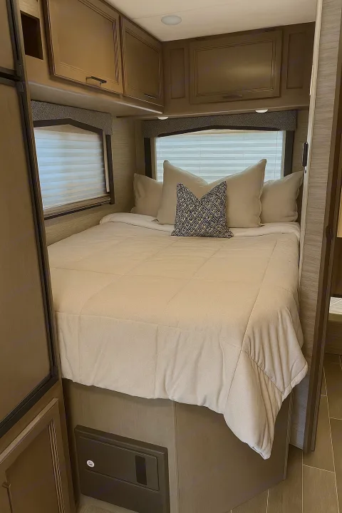 Relax in this cozy RV rental bedroom featuring a comfortable bed, windows with blinds, and convenient overhead storage.. Thor Chateau 2022