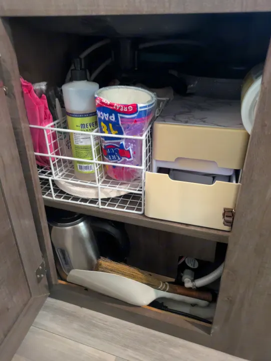 RV rental: Under-sink cabinet with cleaning supplies, paper cups, kettle, and broom, demonstrating smart storage.. Rockwood A122s 2023