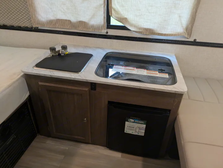 RV rental interior: a compact kitchen with sink, stove, and fridge, bordered by sleeping and seating areas.. Rockwood A122s 2023