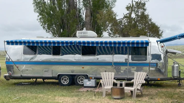 Silver Airstream Excella II RV rental in a green field with a cozy outdoor camping setup.. Airstream Excella 1981
