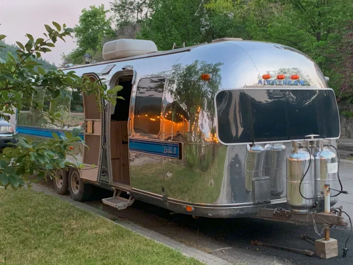 A shiny Airstream Excella II travel trailer, often used for rv rental, parked at dusk with its door open and reflections of lights.. Airstream Excella 1981
