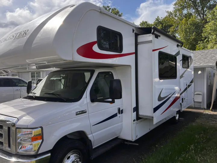 A white Ford Forester Class C RV rental is parked, showcasing its extended slide-out and distinctive red/blue stripes.. Forester Forester Motorhome 2020