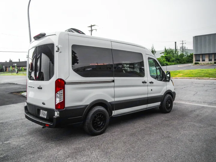 White Ford Transit rv rental, customized for road trips, seen parked on asphalt in an industrial area.. Ford Transit 2019