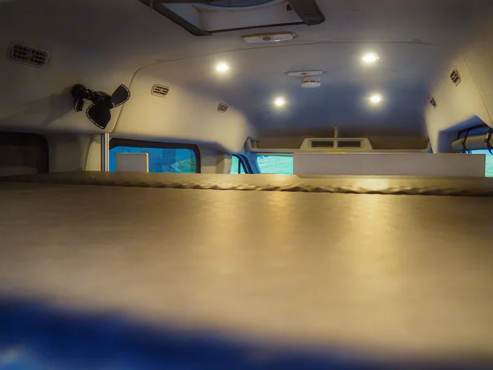 Inside an **RV rental**: a comfy **camper van** bed, ceiling lights, fan, and air vents visible in the modern interior.. Ford Transit 2019