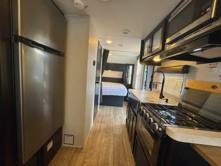Inside a clean RV rental: full kitchen with stove and sink, stainless steel fridge, and a cozy bedroom.. Forest River Grey Wolf Limited 2022