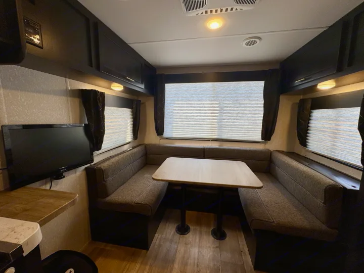 Cozy RV rental dinette features U-shaped seating, a table, TV, and dark overhead cabinets, offering a compact living space.. Forest River Grey Wolf Limited 2022