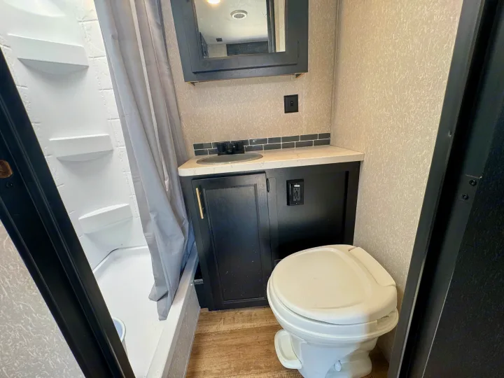 Compact RV rental bathroom: white shower, black vanity with sink, mirror, and toilet.. Forest River Grey Wolf Limited 2022