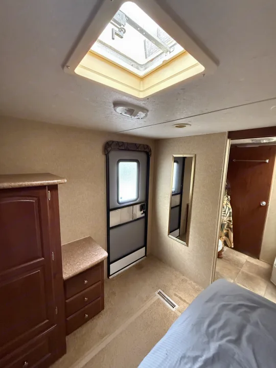 RV rental bedroom view: Features a bright skylight, wood cabinets, entry door, and wall mirror.. Rockwood Signature Ultra Lite 2012
