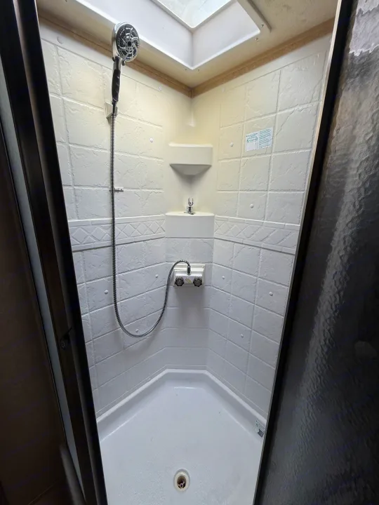 Inside an RV rental: a compact, clean shower with white textured walls, a handheld showerhead, corner shelves, and skylight.. Rockwood Signature Ultra Lite 2012