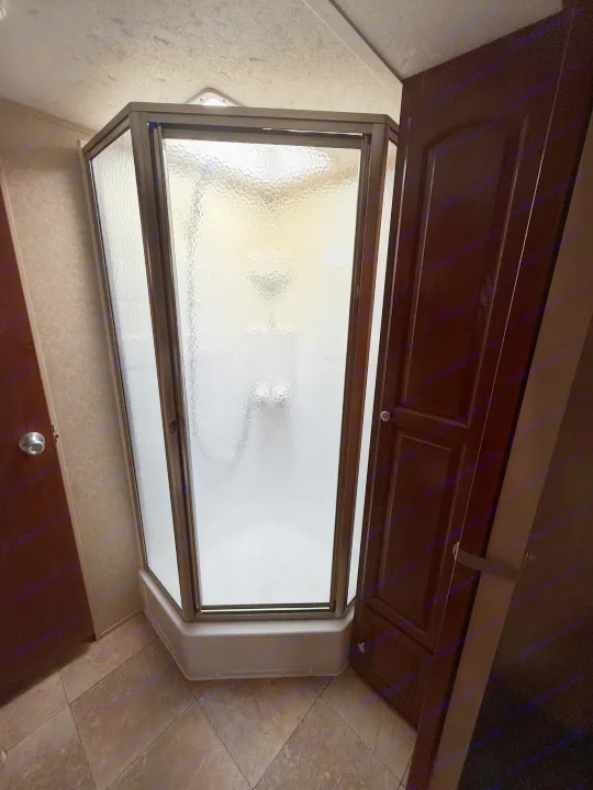 Interior view of an RV rental: a modern, space-saving corner shower with textured glass and nearby cabinet access.. Rockwood Signature Ultra Lite 2012