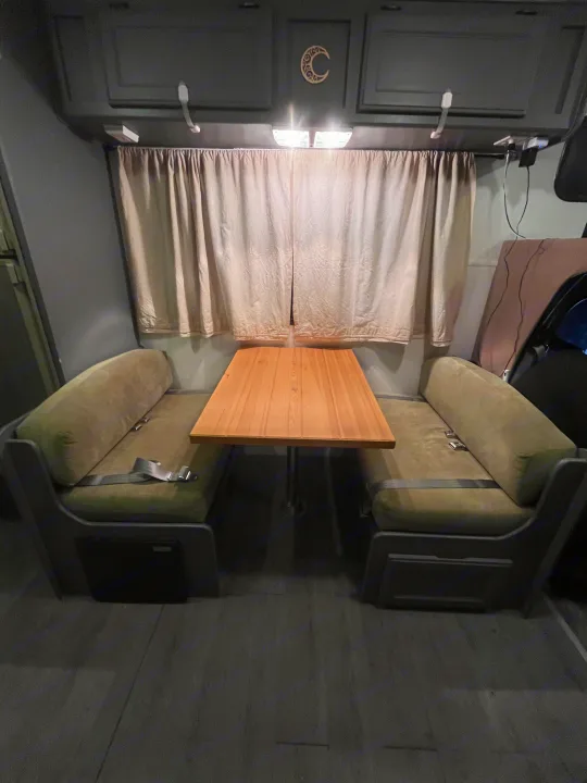 Compact RV rental interior: a cozy dinette with olive green benches, wooden table, and overhead lighting.. Gulf Stream Ultra 1998
