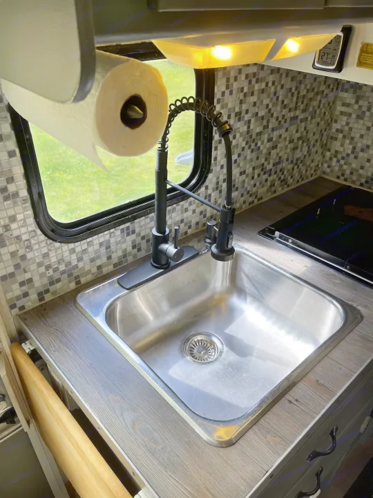 Modern RV rental kitchen with sleek sink, black faucet, tiled backsplash, and green view. Perfect for cooking on the road.. Gulf Stream Ultra 1998