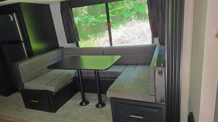 Cozy RV rental interior featuring a U-shaped dinette with grey cushions, black table, and scenic window view.. Forest River Cherokee 2022
