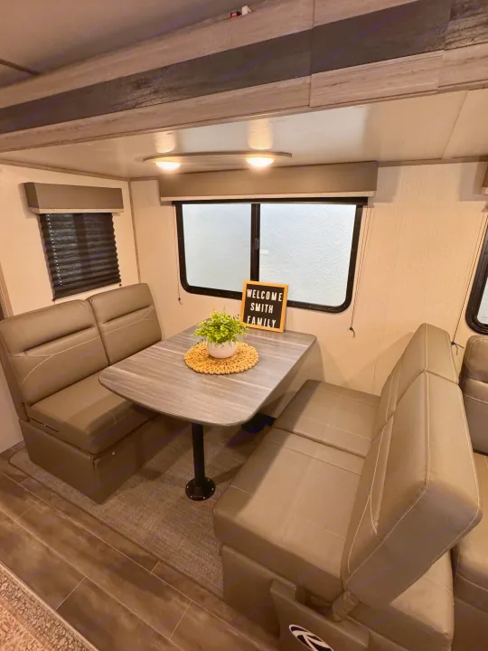 Comfortable RV rental dinette featuring cushioned benches, a table with decor, and a 'Welcome Smith Family' sign.. Keystone RV Passport TT 2022