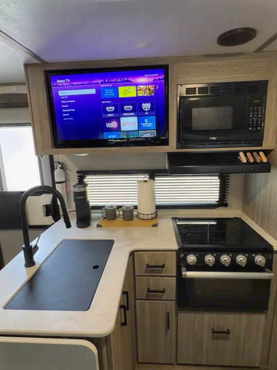 RV rental kitchen with stove, microwave, sink, and Roku TV. Compact yet fully equipped for travel comfort & entertainment.. Keystone RV Passport TT 2022