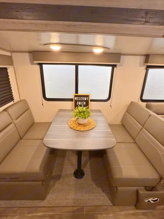 Cozy RV rental interior features a dinette with bench seats, table, 'Welcome Smith' sign and plant.. Keystone RV Passport TT 2022