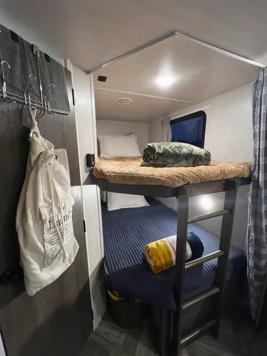 An RV rental's cozy interior, showcasing compact bunk beds with a ladder and comfortable bedding.. Forest River Wildwood X-Lite 2022