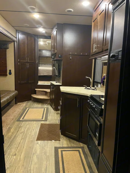 Spacious RV rental interior with kitchen, elevated bedroom, and living space. Features dark cabinetry and modern appliances.. Forest River Wolf Pack 2018