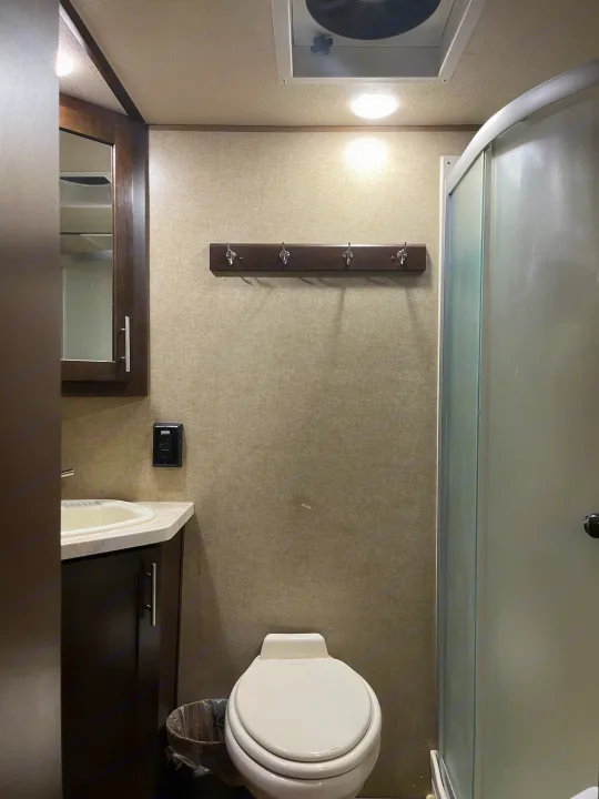 Inside an RV rental bathroom, featuring a compact toilet, vanity with sink, shower, and wall hooks for convenience.. Forest River Wolf Pack 2018