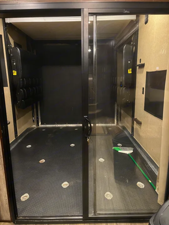 Spacious RV rental toy hauler interior with textured floor, tie-downs, foldable bench, and sliding glass doors.. Forest River Wolf Pack 2018