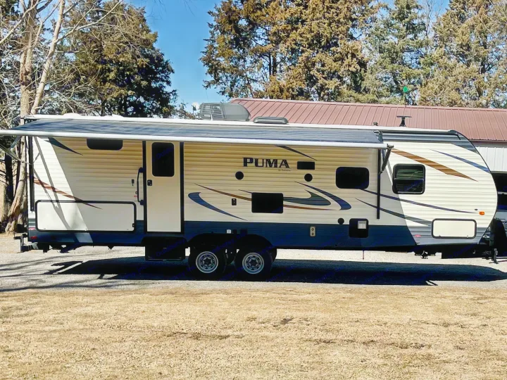 Side view of a PUMA travel trailer RV rental with awning extended, parked on gravel. Perfect for your next trip!. Forest River Palomino Puma 2018