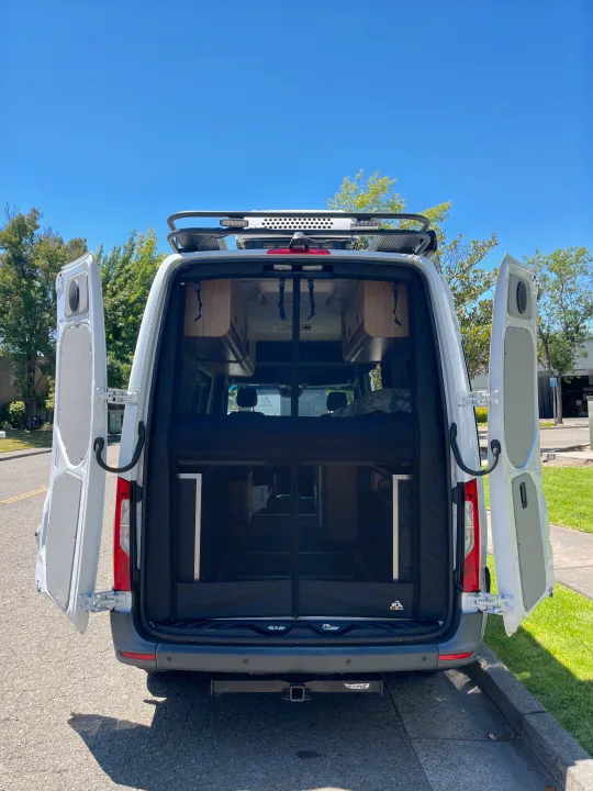 White camper van with open rear doors, showing an interior bug screen and living space. Ideal for RV rental getaways.. Mercedes Sprinter Sprinter 2500 2021