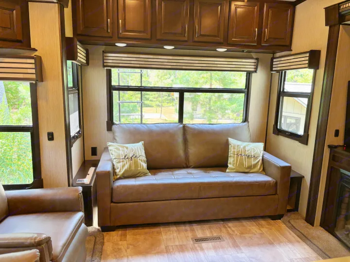 Comfortable RV rental living area featuring a brown sofa with decorative pillows, multiple windows, and overhead cabinets.. 4x4fcmp23h6007284 Columbus 2017