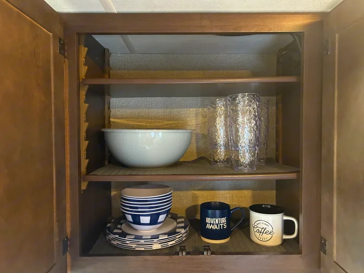RV rental kitchen cabinet showing organized shelves with a large bowl, clear cups, plates, and coffee mugs.. Thor Freedom Elite 2019