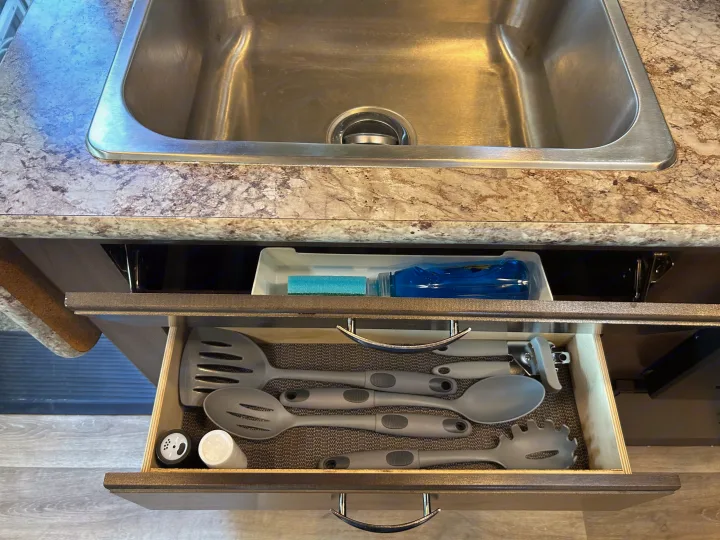 RV rental kitchen setup: stainless steel sink, pull-out drawer with kitchen utensils, and shelf with dish soap.. Thor Freedom Elite 2019