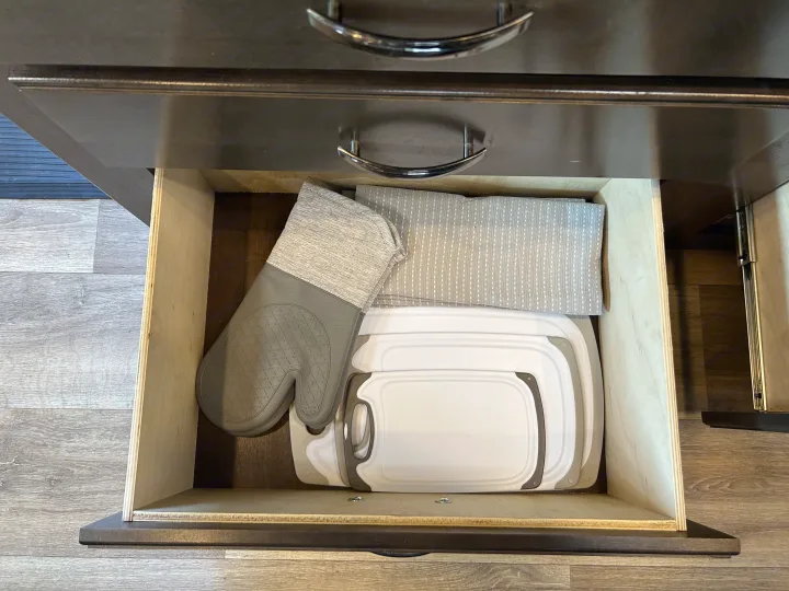 Organized RV rental kitchen drawer with an oven mitt, dish towel, and space-saving cutting boards for compact living.. Thor Freedom Elite 2019