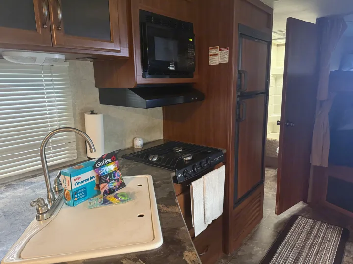 RV rental interior featuring a full kitchen with microwave, stove, sink, and fridge. Ready for s'mores & adventures!. Keystone RV Cougar 2014