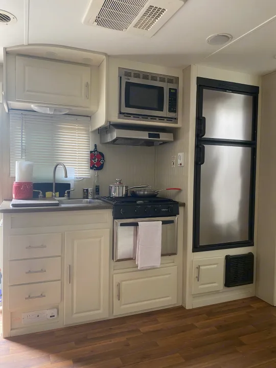 Inside an RV rental: a compact kitchen with sink, microwave, gas range/oven, and a stainless steel refrigerator.. Cruiser RV Fun Finder X 2011