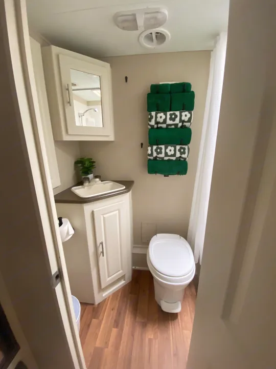 Inside a modern RV rental bathroom, featuring a compact toilet, corner sink, mirror cabinet, and neatly stacked green towels.. Cruiser RV Fun Finder X 2011