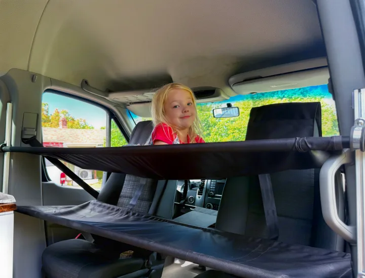 Child peeks from a fabric bunk inside an RV rental van, highlighting clever interior sleeping/storage solutions.. Mercedes-Benz Sprinter 2016