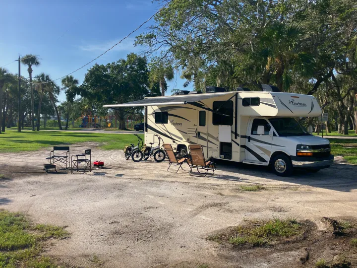 RV rental campsite setup: A motorhome, bikes, chairs, and a fire pit await outdoor fun near a playground.. Forest River Coachmen Freelander 2017