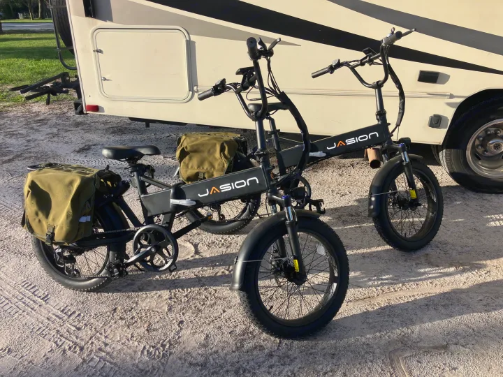 Two Jasion folding e-bikes, one with storage bags, parked on sand by an RV rental, great for exploring.. Forest River Coachmen Freelander 2017