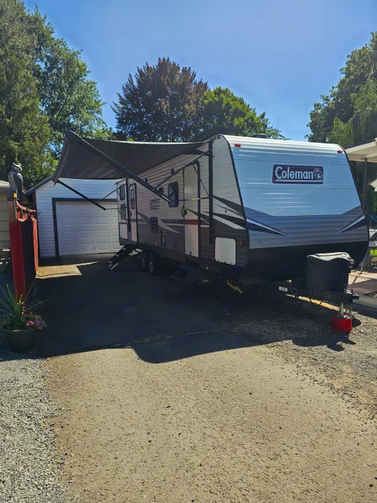 Sunny day with a parked Coleman travel trailer, awning extended. Explore RV rental options for your outdoor adventures!. Dutchmen Coleman Lantern 2021