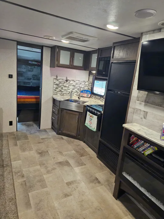 Spacious RV rental interior featuring a modern kitchen, cozy living area with TV/fireplace, and bedroom access. Ideal for camper adventures!. Dutchmen Coleman Lantern 2021