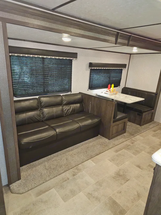 Inside this RV rental: black leather sofa, dinette with table & condiments, blinds, and carpet/tile flooring.. Dutchmen Coleman Lantern 2021