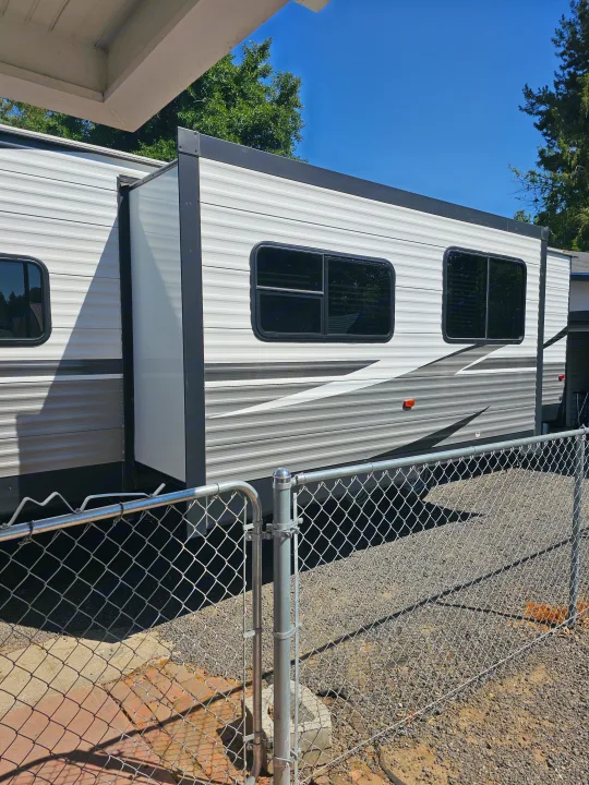 White & gray RV rental with extended slide-out, parked outdoors behind a chain-link fence on a sunny day.. Dutchmen Coleman Lantern 2021