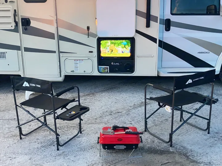 An RV rental provides outdoor entertainment with a TV, two camping chairs, and a grill on snowy ground.. Forest River Coachmen Freelander 2017