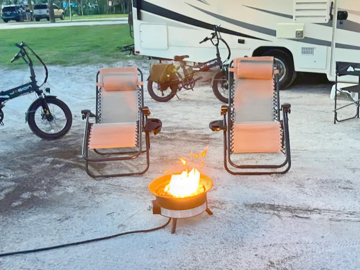 Cozy RV rental campsite at dusk, featuring a portable fire pit, two lounge chairs, and two electric bikes.. Forest River Coachmen Freelander 2017