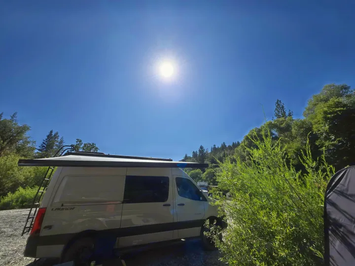 Bright day with an RV rental camper van parked in a sunny natural setting, surrounded by trees under a clear blue sky.. Entegra Launch Sprinter High Roof AWD 4x4 Camper Van 2025