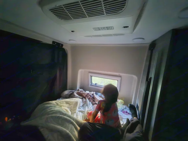 Inside a cozy RV rental: A child sits on the bed looking out the window at trees. Comfort for family travel.. Entegra Launch Sprinter High Roof AWD 4x4 Camper Van 2025