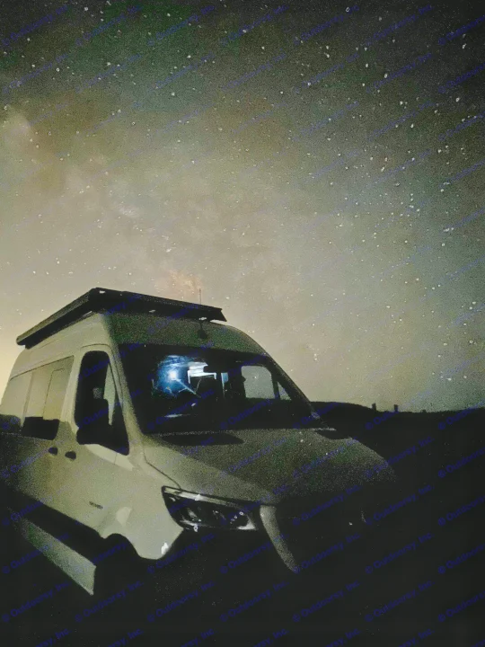 An RV rental van sits under a vivid Milky Way night sky, with a light illuminating its interior, ideal for camping adventures.. Entegra Launch Sprinter High Roof AWD 4x4 Camper Van 2025